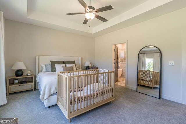 bedroom with carpet floors, ensuite bath, a tray ceiling, and ceiling fan