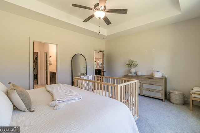 carpeted bedroom with ensuite bathroom, ceiling fan, and a tray ceiling