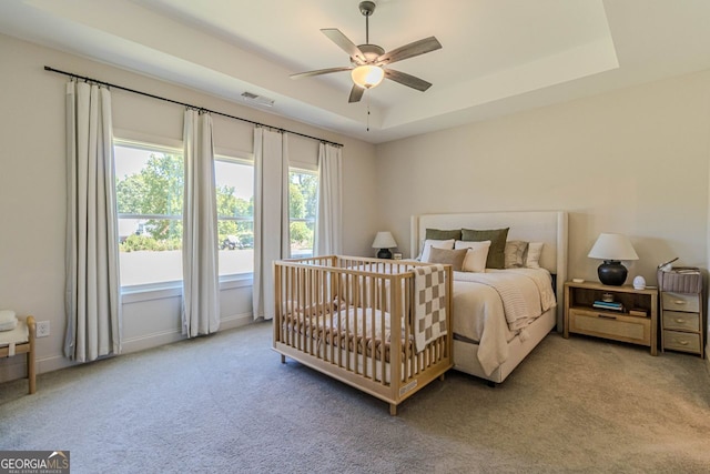 bedroom featuring ceiling fan, carpet flooring, a nursery area, and a tray ceiling