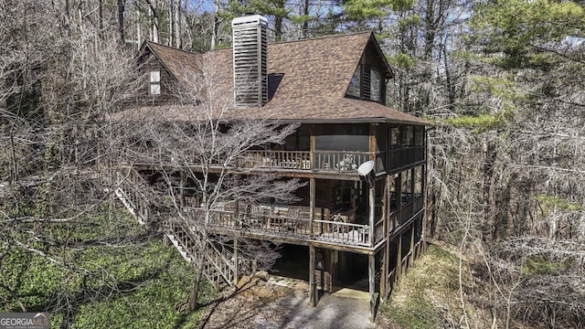 view of property exterior featuring a shingled roof, a chimney, and a wooden deck