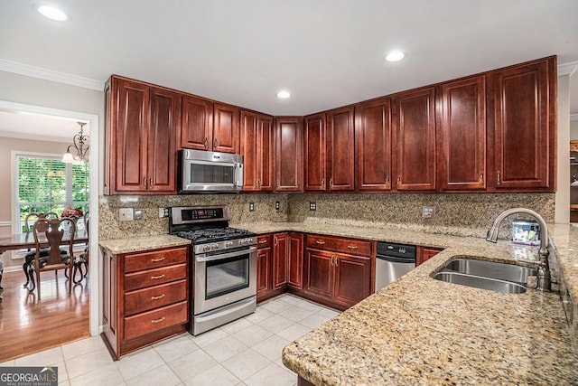 kitchen with light stone countertops, sink, a notable chandelier, appliances with stainless steel finishes, and ornamental molding