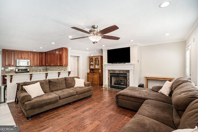 living room with ceiling fan, dark hardwood / wood-style flooring, crown molding, and a high end fireplace