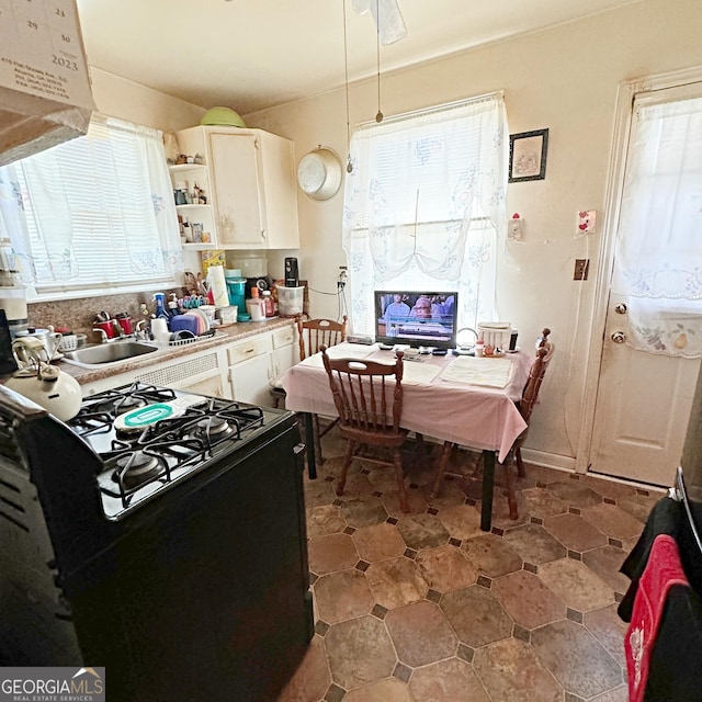 kitchen featuring black gas range oven, white cabinetry, and sink