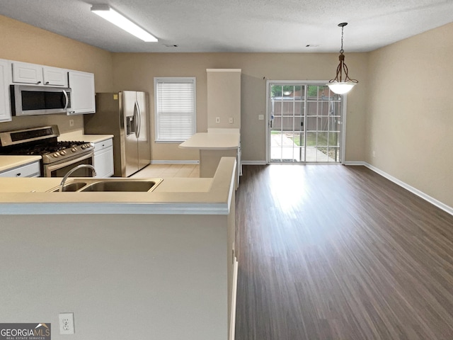 kitchen with appliances with stainless steel finishes, decorative light fixtures, wood-type flooring, sink, and white cabinets