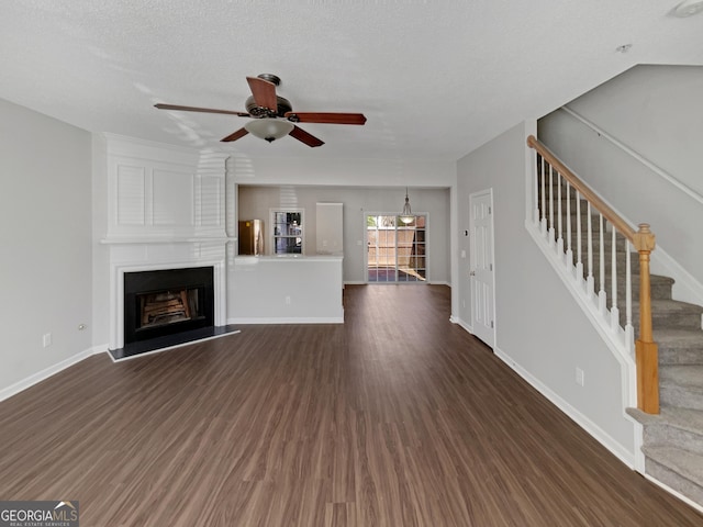 unfurnished living room with baseboards, ceiling fan, dark wood finished floors, stairway, and a fireplace