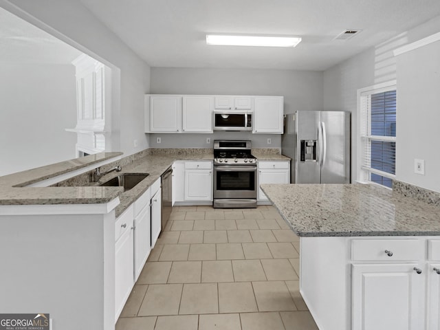 kitchen featuring a sink, light stone counters, appliances with stainless steel finishes, and a peninsula