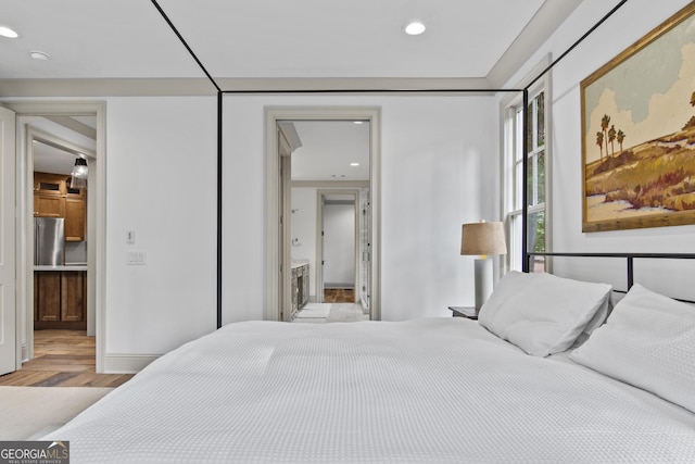 bedroom with light hardwood / wood-style floors, stainless steel refrigerator, and ensuite bath