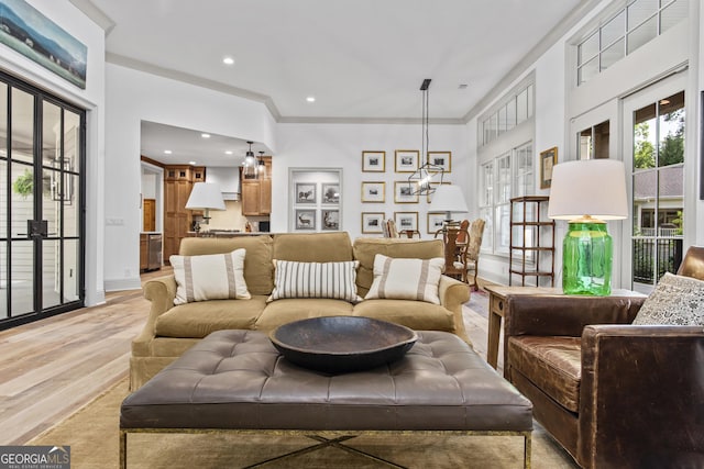 living room featuring crown molding, french doors, light hardwood / wood-style floors, and an inviting chandelier