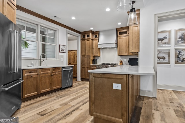 kitchen featuring high end black fridge, premium range hood, sink, hanging light fixtures, and stainless steel dishwasher