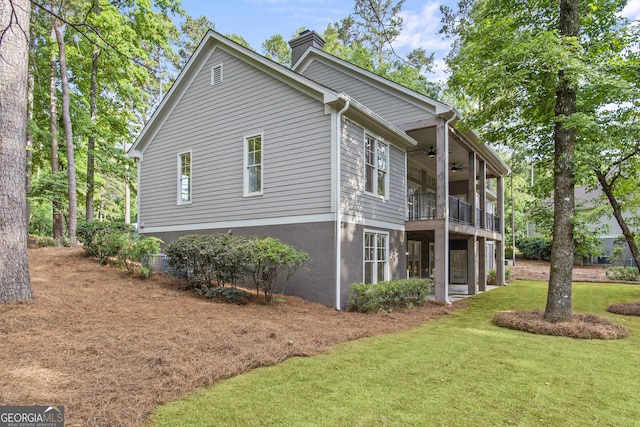 view of side of home with ceiling fan, a balcony, and a yard