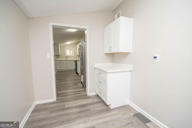 corridor featuring vaulted ceiling, sink, and light hardwood / wood-style floors