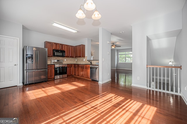 kitchen with appliances with stainless steel finishes, hanging light fixtures, dark wood-type flooring, tasteful backsplash, and ceiling fan with notable chandelier