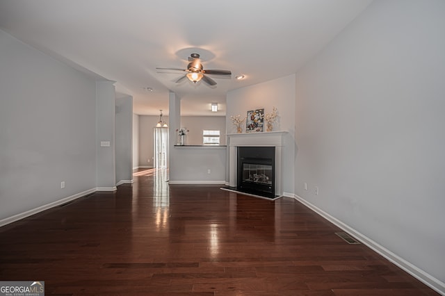 unfurnished living room with ceiling fan with notable chandelier and dark wood-type flooring