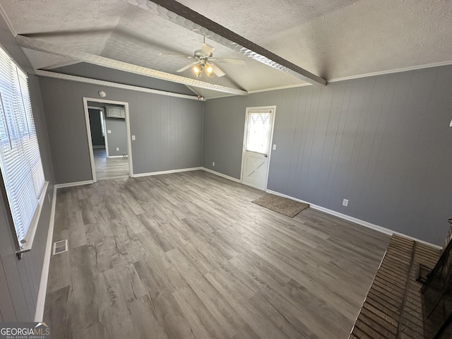 empty room featuring a textured ceiling, ceiling fan, wooden walls, hardwood / wood-style floors, and vaulted ceiling with beams