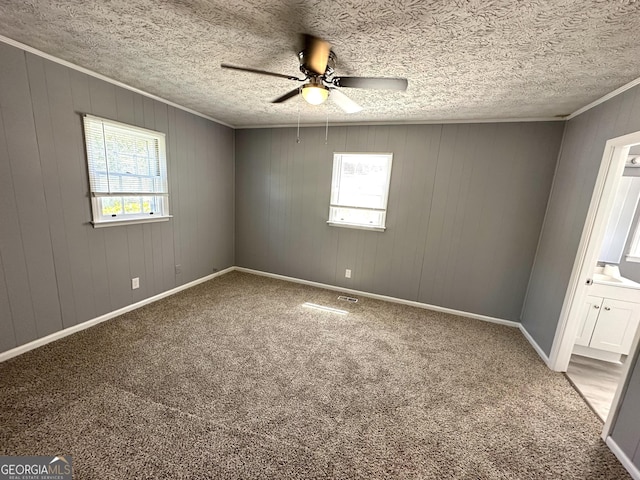 carpeted empty room featuring ceiling fan, wood walls, and a textured ceiling