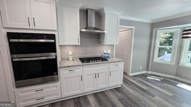 kitchen featuring white cabinets, ornamental molding, multiple ovens, wall chimney range hood, and stainless steel gas stovetop