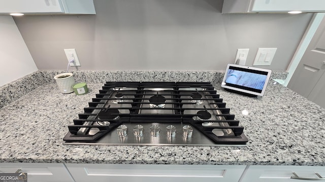 details with light stone counters, white cabinetry, and stainless steel gas stovetop