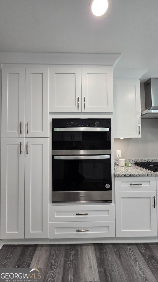 kitchen with double oven, black gas stovetop, white cabinetry, wall chimney range hood, and light stone countertops