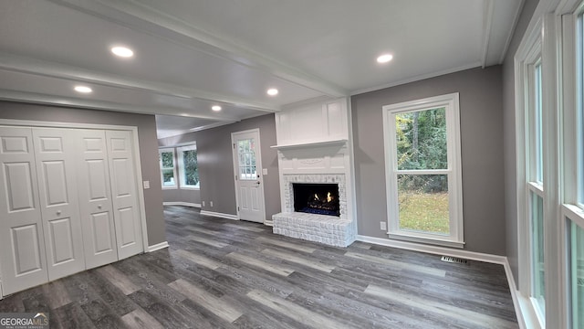 living room with beam ceiling, dark hardwood / wood-style flooring, a brick fireplace, and crown molding