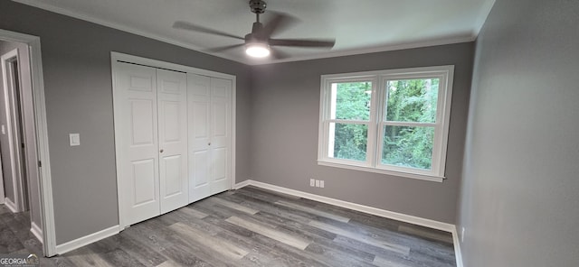 unfurnished bedroom featuring dark wood-style flooring, a ceiling fan, baseboards, a closet, and crown molding