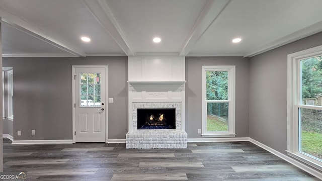 unfurnished living room featuring beam ceiling, dark hardwood / wood-style floors, a brick fireplace, and ornamental molding