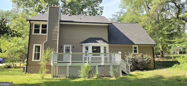 back of property with a chimney, a deck, a lawn, and roof with shingles