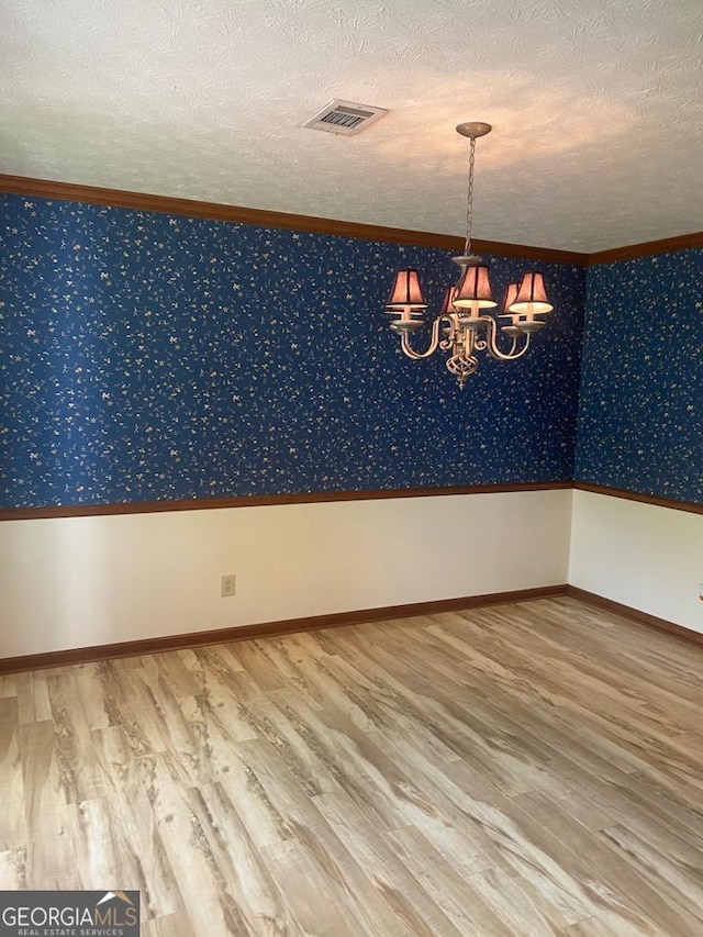 spare room with hardwood / wood-style floors, ornamental molding, a chandelier, and a textured ceiling