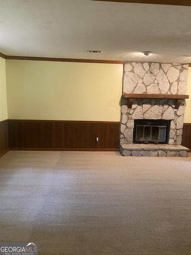 unfurnished living room with a stone fireplace, wood walls, crown molding, a textured ceiling, and carpet floors