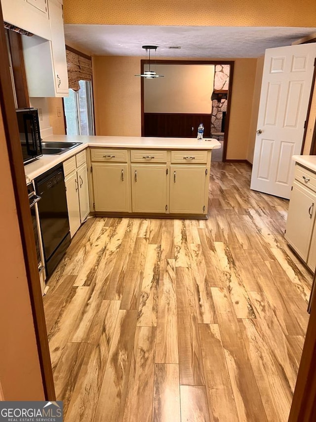 kitchen with pendant lighting, kitchen peninsula, sink, black appliances, and light hardwood / wood-style flooring