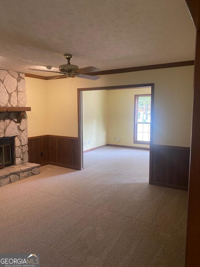 unfurnished living room with crown molding, ceiling fan, carpet, a textured ceiling, and a stone fireplace