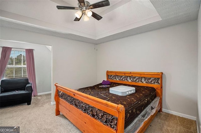 carpeted bedroom featuring a tray ceiling, ceiling fan, and a textured ceiling