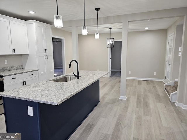 kitchen featuring white cabinetry, sink, hanging light fixtures, light stone counters, and a kitchen island with sink