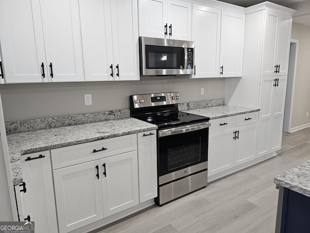 kitchen with light stone counters, light wood-type flooring, white cabinetry, and stainless steel appliances