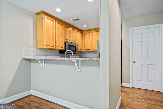 kitchen featuring a kitchen bar, kitchen peninsula, backsplash, light stone countertops, and light hardwood / wood-style floors