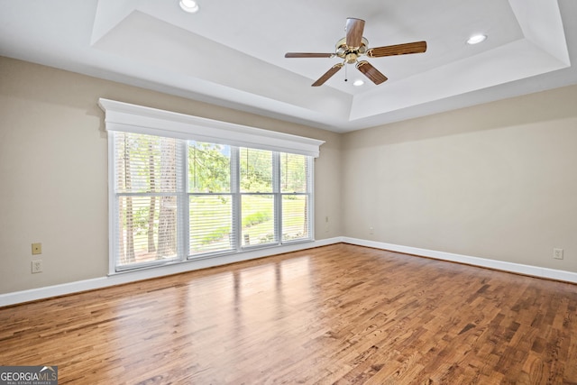 spare room with hardwood / wood-style flooring, ceiling fan, and a raised ceiling