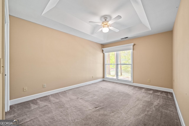 empty room with carpet flooring, ceiling fan, and a tray ceiling