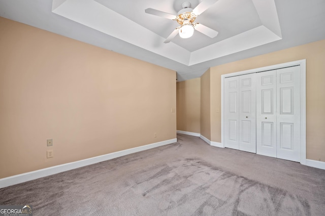 unfurnished bedroom featuring carpet, ceiling fan, a closet, and a tray ceiling