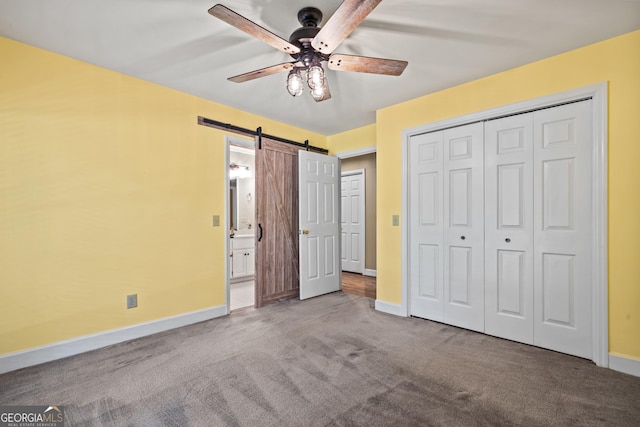 unfurnished bedroom with ensuite bathroom, ceiling fan, a barn door, carpet floors, and a closet