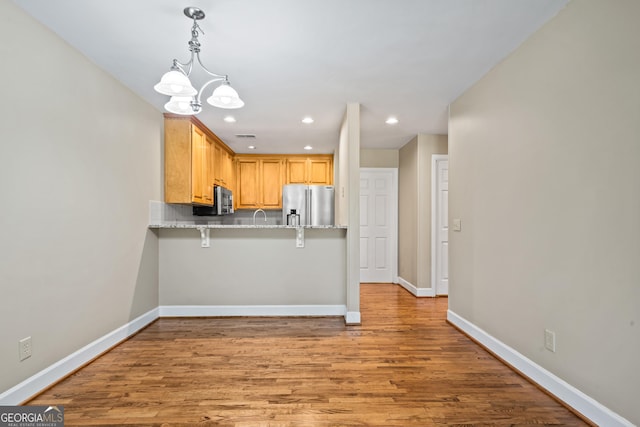 kitchen with kitchen peninsula, appliances with stainless steel finishes, tasteful backsplash, a breakfast bar, and decorative light fixtures