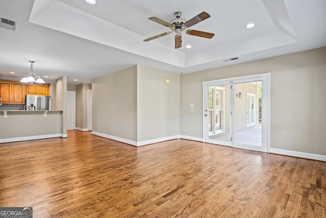 unfurnished living room featuring a raised ceiling, wood-type flooring, and ceiling fan with notable chandelier