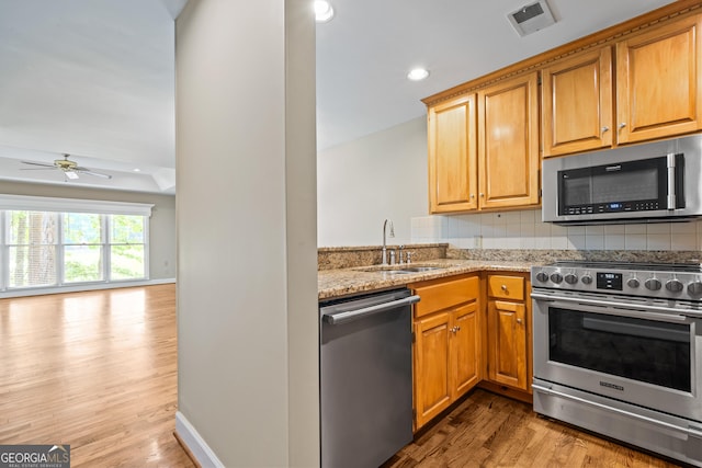 kitchen featuring decorative backsplash, appliances with stainless steel finishes, light stone counters, sink, and light hardwood / wood-style floors