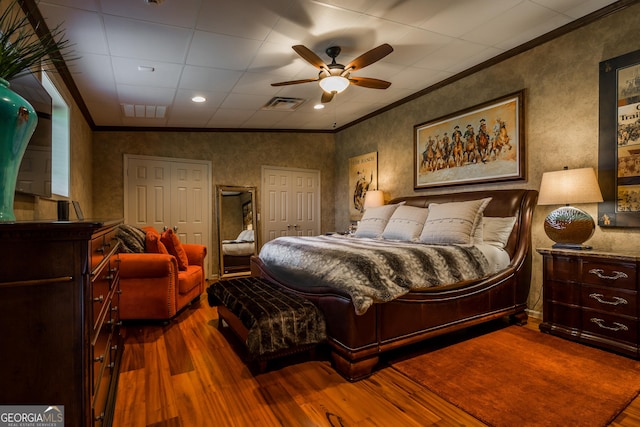 bedroom with ceiling fan, wood-type flooring, ornamental molding, and two closets