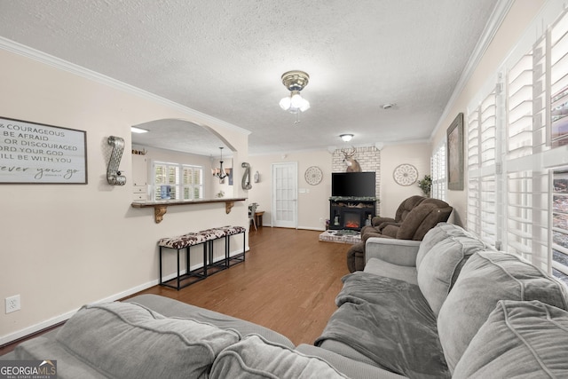 living room featuring an inviting chandelier, crown molding, a fireplace, a textured ceiling, and dark hardwood / wood-style flooring