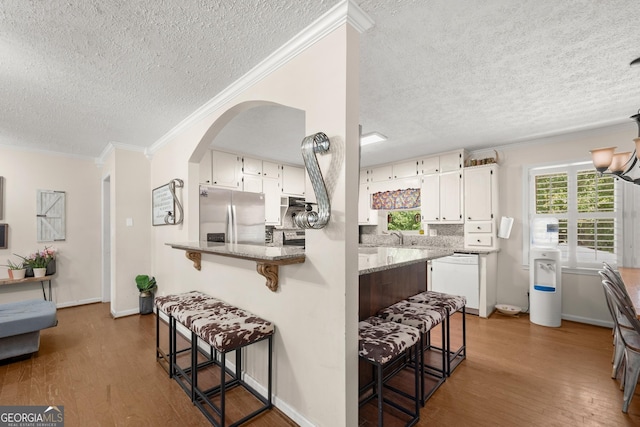 kitchen featuring stone counters, white dishwasher, kitchen peninsula, stainless steel fridge, and white cabinetry