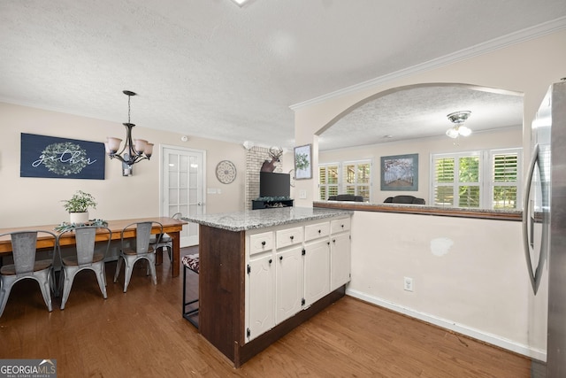 kitchen with white cabinetry, light stone countertops, an inviting chandelier, stainless steel fridge, and a textured ceiling