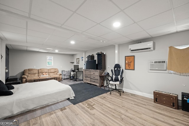 bedroom with a drop ceiling, light wood-type flooring, and an AC wall unit