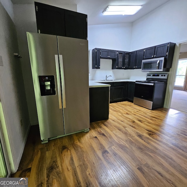 kitchen with appliances with stainless steel finishes, light hardwood / wood-style floors, sink, and high vaulted ceiling