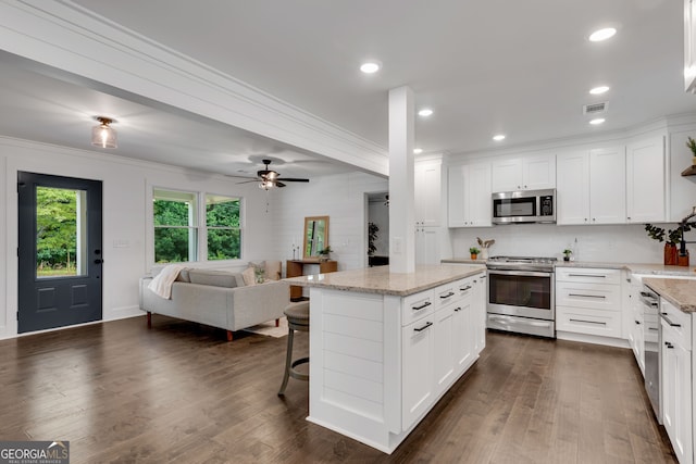 kitchen featuring white cabinetry, a center island, stainless steel appliances, a kitchen breakfast bar, and light stone counters