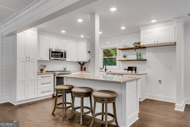 kitchen with light stone countertops, stainless steel appliances, a kitchen island, a breakfast bar, and white cabinets