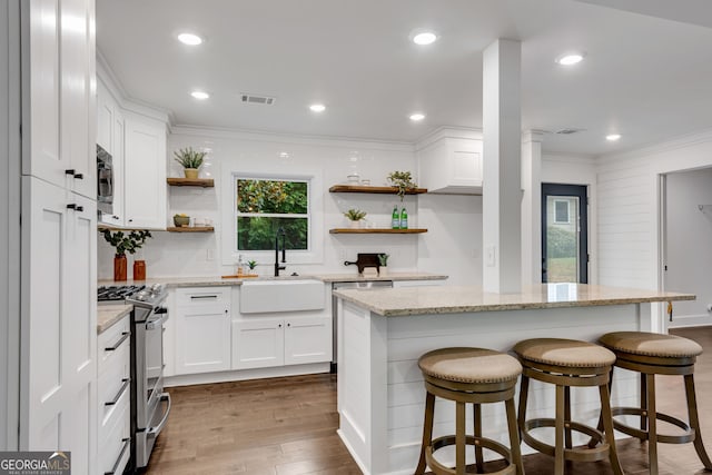 kitchen with sink, a kitchen island, light stone counters, white cabinetry, and stainless steel appliances